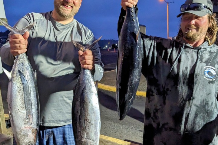 two men smiling holding up two albacore tuna