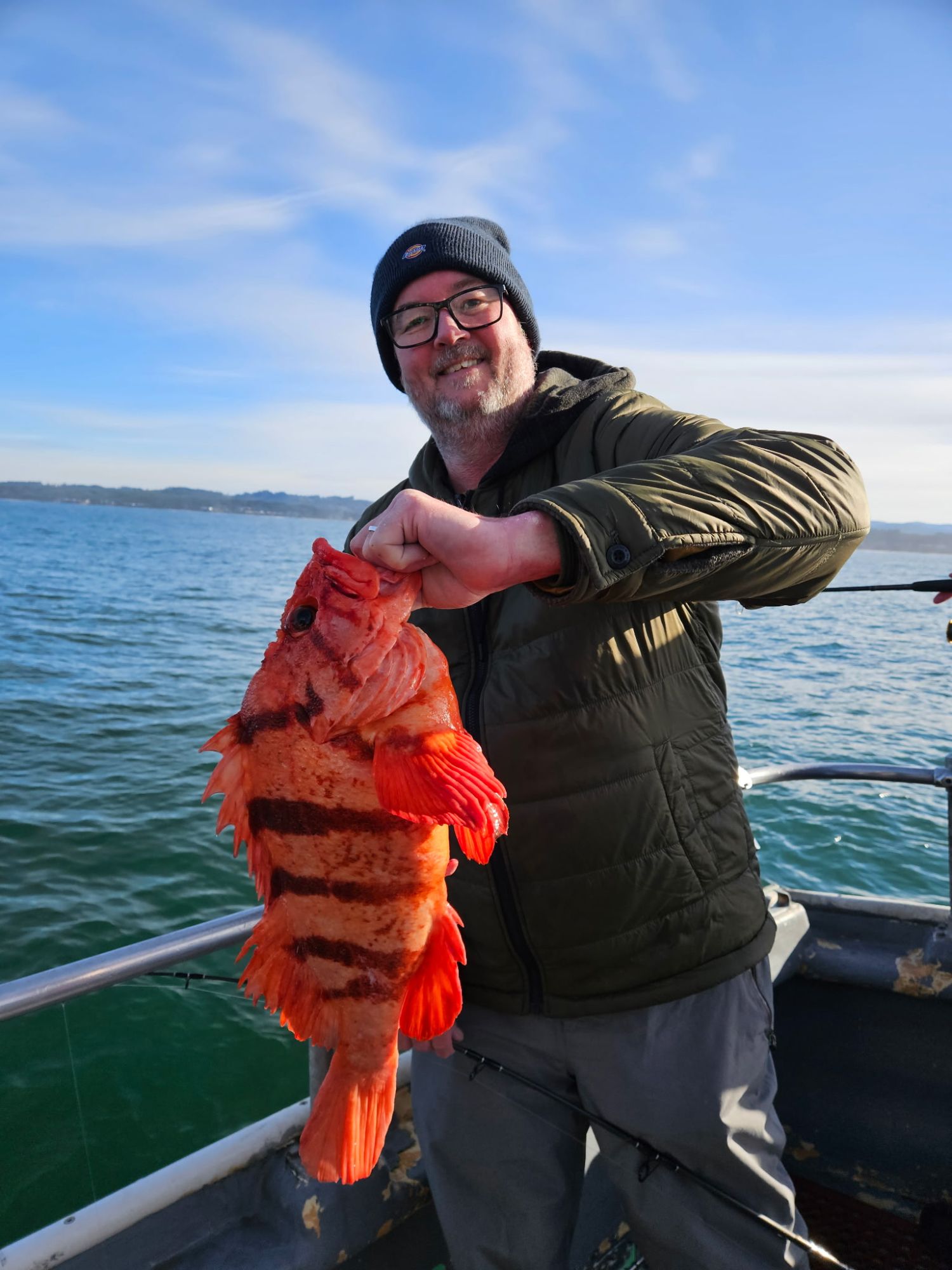 Person holding a large, striped orange fish on a boat with ocean in the background.