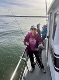Person holding a fish on a boat with fishing gear and calm sea.