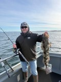Man on boat holds fishing rod and large fish, ocean in background.