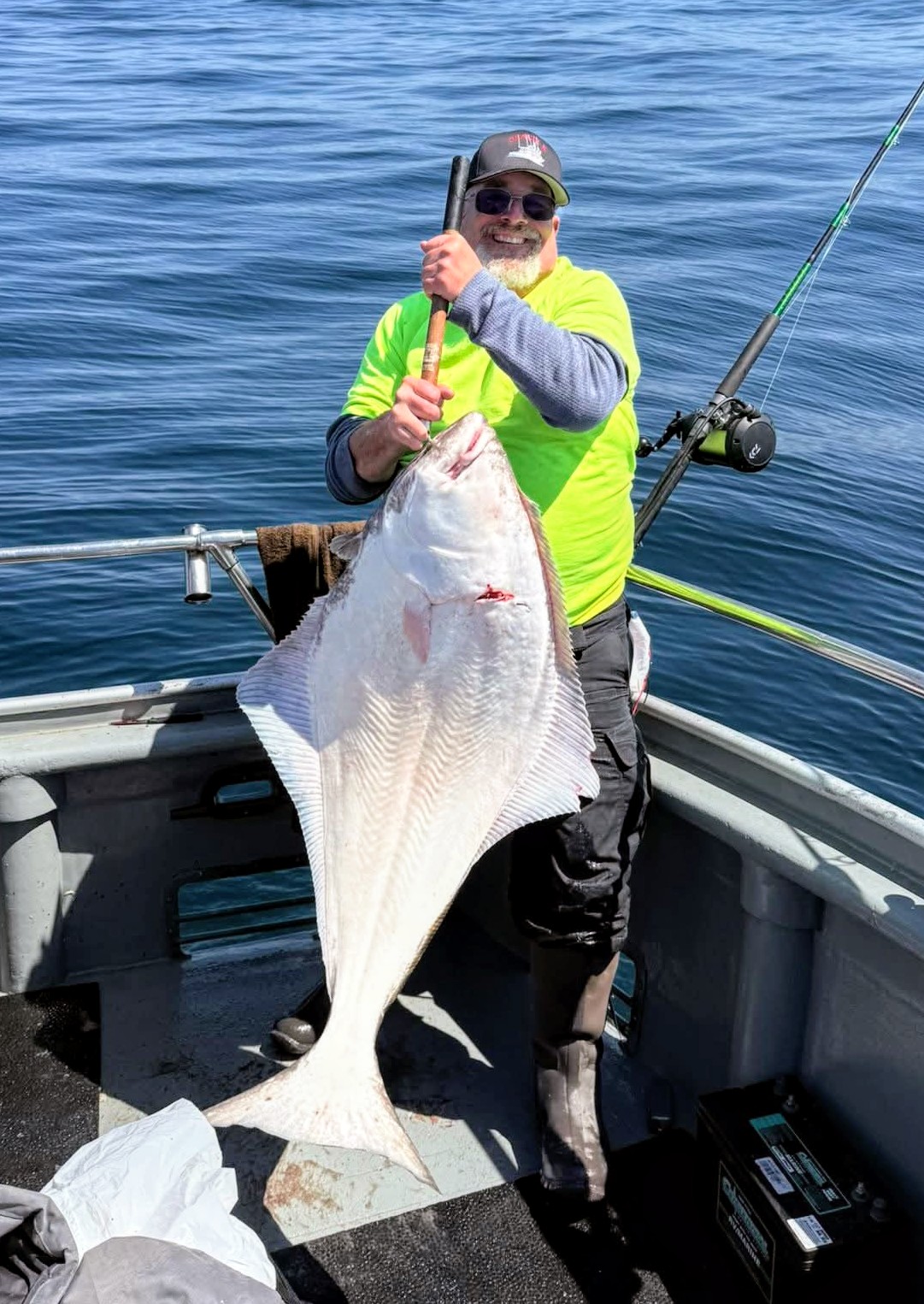 Person on a boat holding a large flat fish with fishing rod in background.