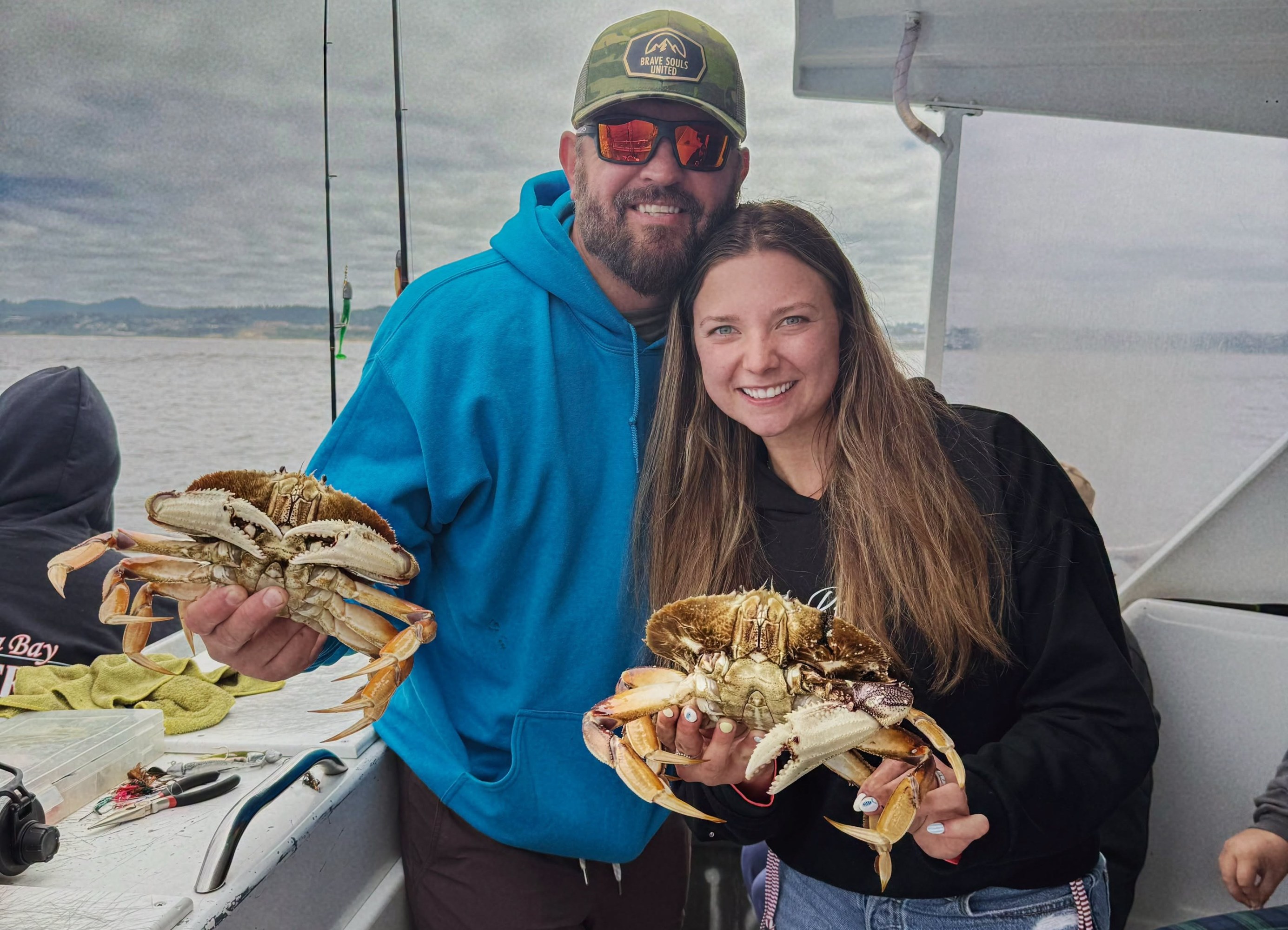 Two people on a boat holding big crabs, smiling at the camera.